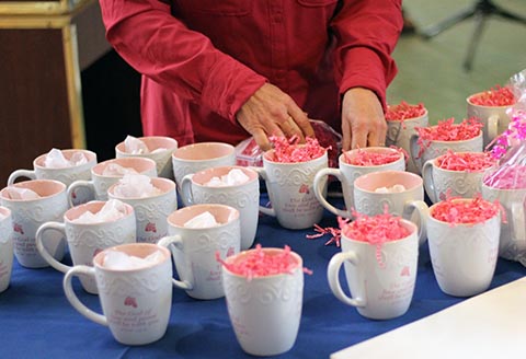 Many mugs being filled with crinkle paper by a woman for a Mother's Day service project.